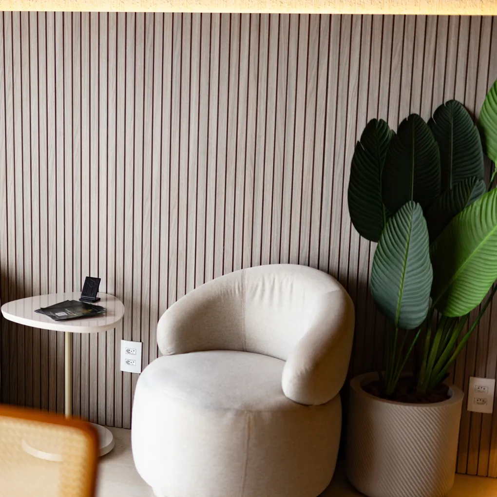 Parede em painel ripado claro com poltrona e mesa de apoio
