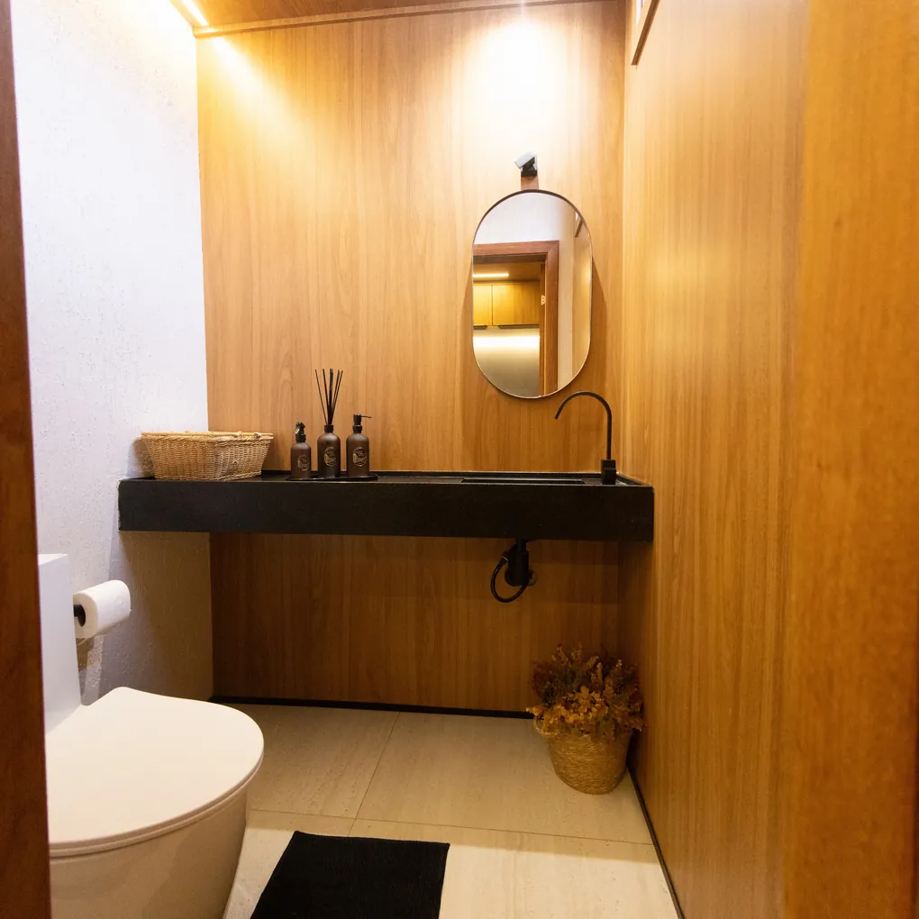 Lavabo revestido em madeira com bancada em granito preto e espelho oval